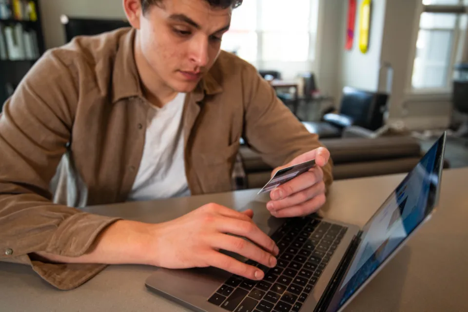 Homem a pagar uma compra online com o cartão, em frente ao portátil.